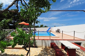 A swimming pool with a slide, surrounded by a white wall, with a stone patio and a red bench.