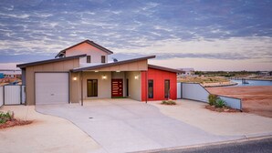 Ein modernes, zweistöckiges Haus mit Garage, rotem Eingangsbereich und Auffahrt zu einem Schwimmbad.