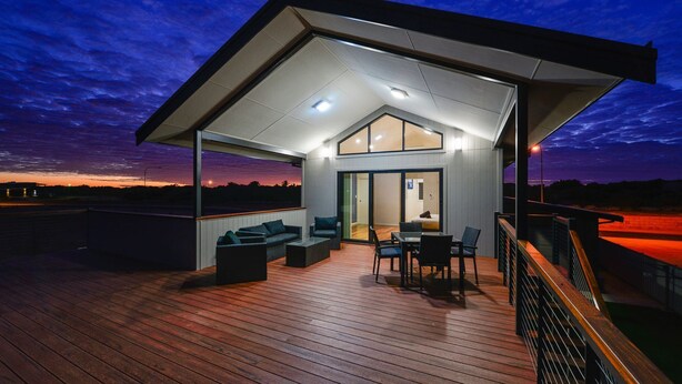 Ein modernes Haus mit überdachter Terrasse, großen Fenstern und Blick auf den Sonnenuntergang.