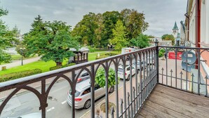 Un balcon donnant sur une rue, des voitures garées et un parc avec des arbres.
