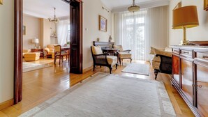 Un vaste salon doté d’un parquet, d’un grand tapis blanc, d’un piano et d’un coin repas avec une table et des chaises.