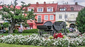 Une calèche traditionnelle, placée au milieu d’un parterre de fleurs, avec un bâtiment à toit rouge en arrière-plan.