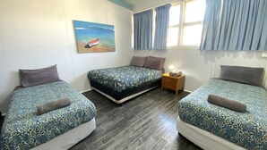 Ein Zimmer mit zwei Einzelbetten, einem Nachttisch, einem Bild von einem Boot auf dem Wasser und einem Fenster mit Vorhängen.