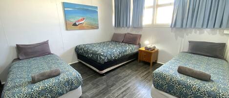 A room with two single beds, a nightstand, a painting of a boat on water, and a window with curtains.