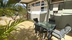 Relax in this serene patio area with a glass-top table and two chairs, surrounded by a tile-paved space and a white lattice fence.