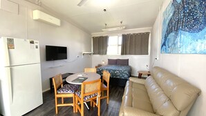 Ein kleines Zimmer mit einem Bett, einer Couch, einem Esstisch mit Stühlen, einem an der Wand montierten Fernseher und einem Wandbild.