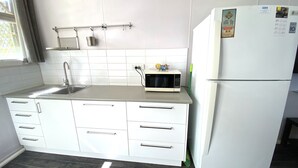 Eine Küche mit weißen Schränken, einer Edelstahl-Spüle, einer Mikrowelle und einem Kühlschrank.
