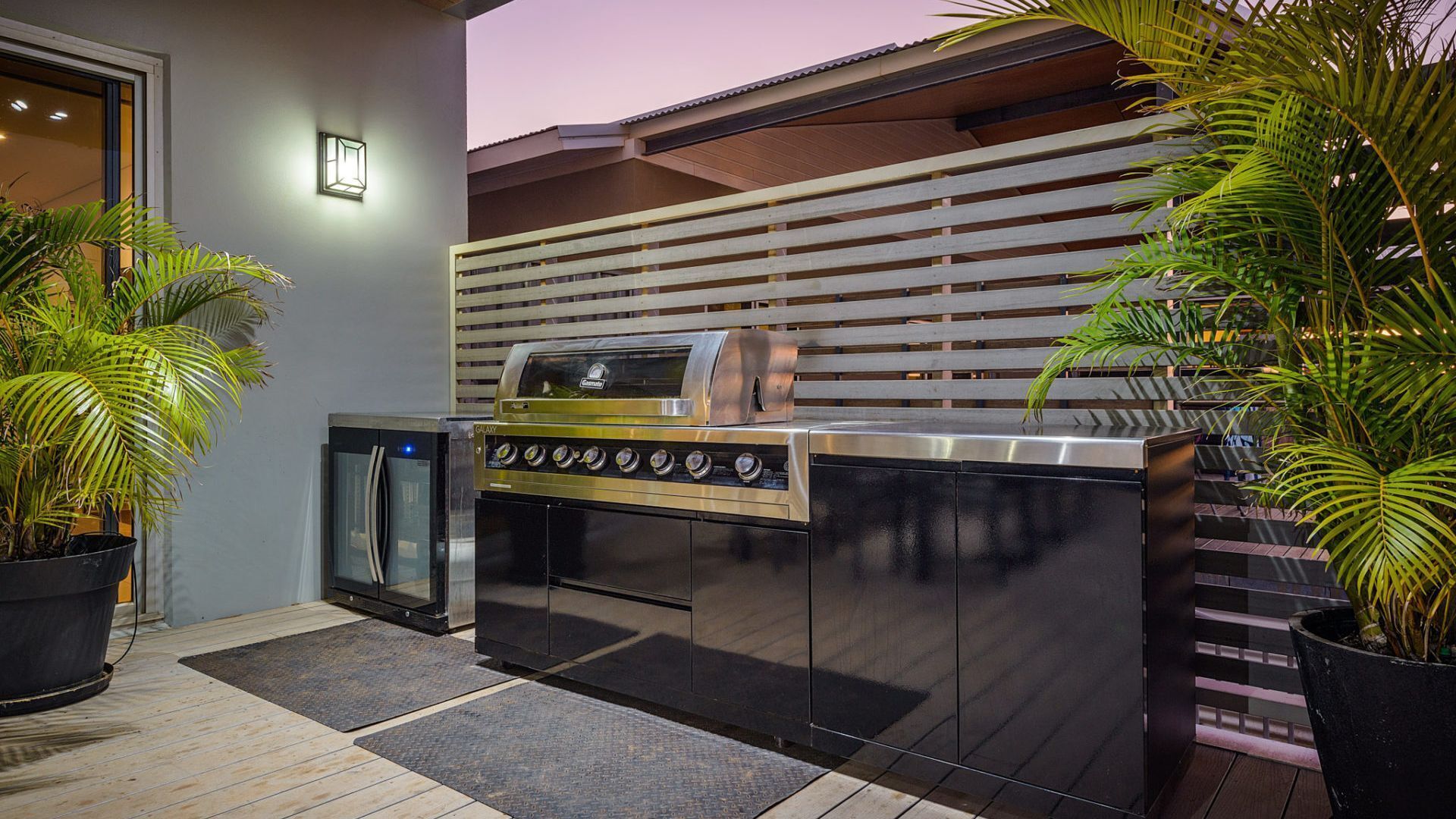 An outdoor kitchen with a built-in grill, a refrigerator, and potted plants.