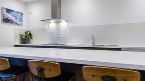 Een moderne keuken met een wit aanrecht, een roestvrijstalen spoelbak en een afzuigkap. Er staan twee houten stoelen met metalen poten bij het aanrecht.