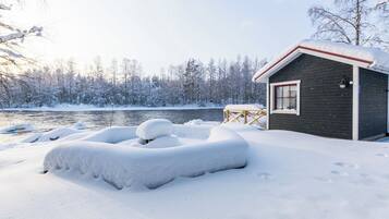 Une cabane dotée d’une petite terrasse et d’une fenêtre, entourée d’un paysage enneigé et d’arbres.