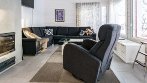 Un salon moderne avec un canapé d’angle, un fauteuil sombre, une table basse en verre et une cheminée.