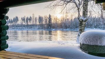 A wooden deck overlooking a snow-covered lake with trees and a cabin in the background.