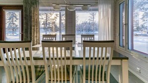 Un coin repas avec une table et des chaises, de grandes fenêtres équipées de stores et une vue sur un paysage enneigé.