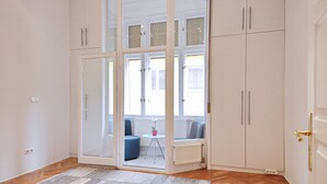 A room with a large sliding glass door leading to a balcony, white cabinets, a small round table with a plant, and a blue chair. - Unique and central apartment in a quiet side street (IX. kerület)
