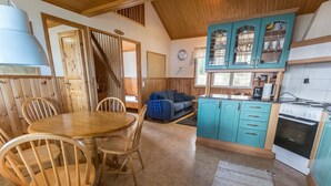 Une cuisine chaleureuse avec des meubles en bois, une table à manger avec des chaises, et un canapé bleu dans une pièce aux murs en bois et au plafond en pente.
