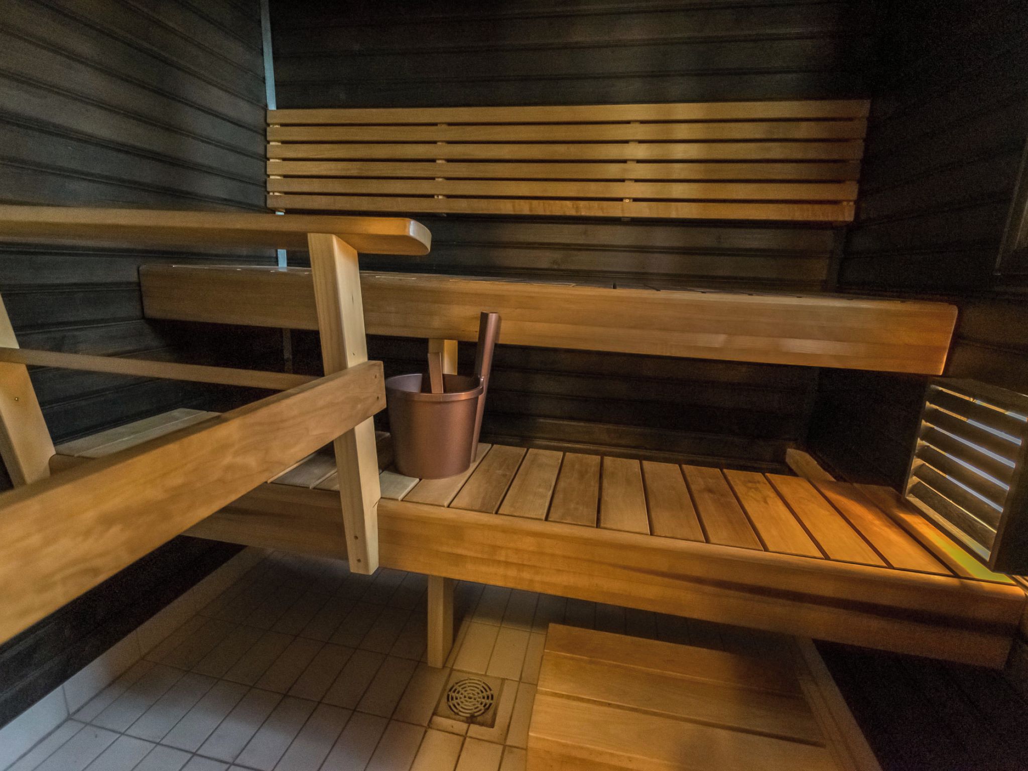 A sauna with wooden benches and a metal bucket.