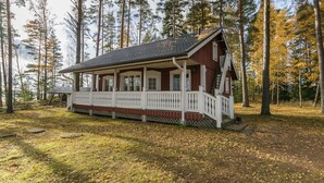 Une cabane dotée d’un porche, entourée d’arbres et bordée d’une pelouse.