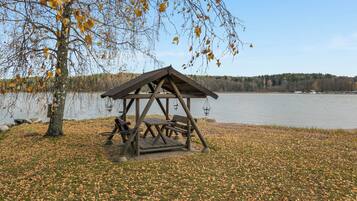 En träbeklädd picknickplats vid en sjö, med bänkar och en gunga, omgiven av höstlöv.