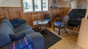 Un salon chaleureux avec un canapé, deux fauteuils en osier, une table en verre et une cheminée.