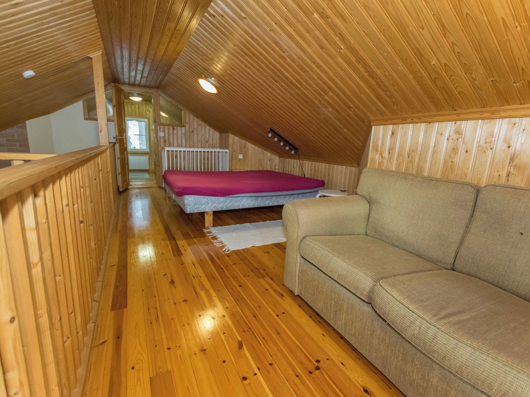 A wooden interior with a bunk bed, a sofa, and a wooden railing.