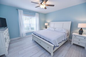 A bedroom with a bed, nightstands, a TV, and a ceiling fan.