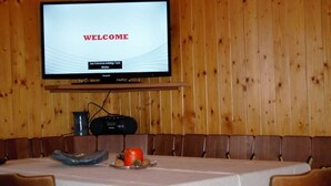 A wooden-paneled room with a television displaying "WELCOME" and a table with a white tablecloth, a plate with food, and a remote control.