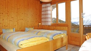 A wooden cabin bedroom with a large bed, a hanging light fixture, and a window with a view of mountains.