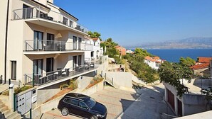 A multi-story residential building with balconies, a car parked in front, and a view of the sea and mountains in the background. - Molo Lozna by Interhome (Brač/Postira)
