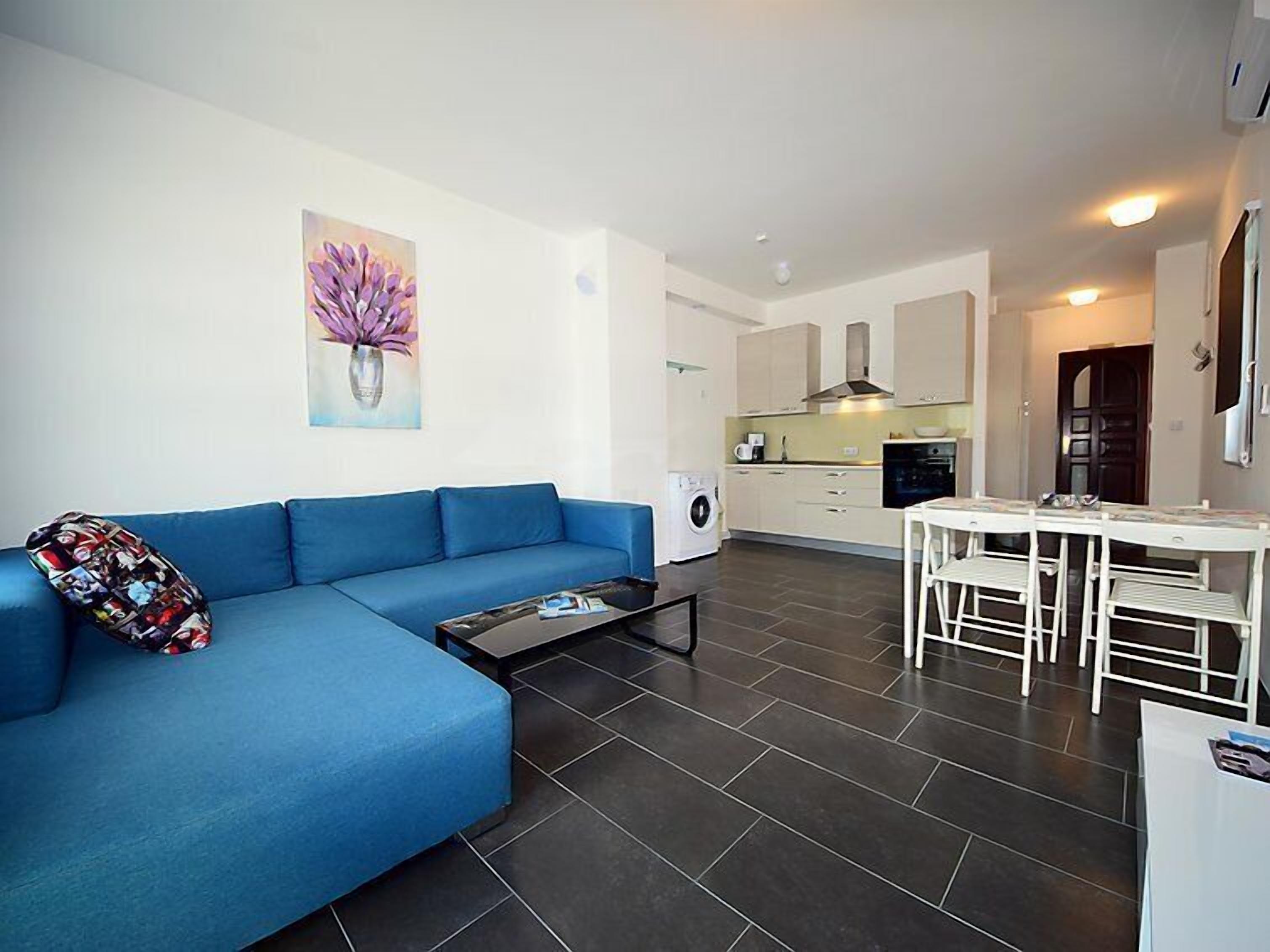 A modern living room with a blue sofa, a coffee table, and a painting of purple flowers.