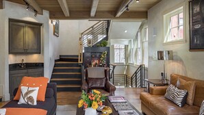 A spacious living room with a sofa, a coffee table with decorative items, a fireplace, and a staircase leading to an upper level. - RIVER BLISS- New Hot Tub, Private, Convenient, & Perfect Location (Telluride)