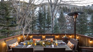 An outdoor dining area with a table set for four, surrounded by wicker chairs, a wooden deck, and a view of a forested area. - RIVER BLISS- New Hot Tub, Private, Convenient, & Perfect Location (Telluride)