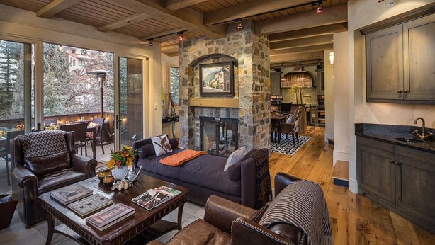 A cozy living room with a stone fireplace, leather furniture, and large windows overlooking a snowy landscape. - RIVER BLISS- New Hot Tub, Private, Convenient, & Perfect Location (Telluride)