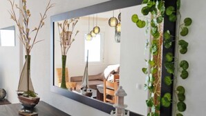Una sala de estar moderna con una mesa de centro de madera oscura, un espejo grande que refleja la habitación, y una planta verde en la pared.