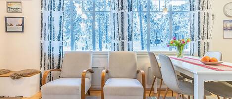 Un comedor con mesa, sillas y vistas a árboles nevados a través de amplias ventanas.