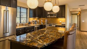 A modern kitchen with dark cabinets, stainless steel appliances, a large granite island, and pendant lighting.