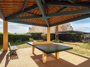 Eine Gartenpatio mit einem grünen Tisch und einer Bank, umgeben von einer Hecke und einem Gebäude im Hintergrund.