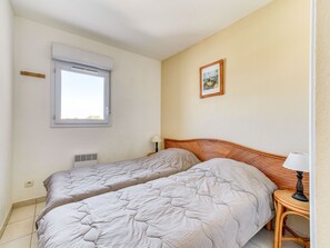 Ein Schlafzimmer mit zwei Betten, einem Fenster, einem Bild an der Wand und einem Nachttisch mit einer Lampe.