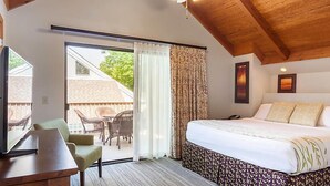 Une chambre dotée d’un grand lit, d’un bureau et d’une porte-fenêtre coulissante donnant sur un espace extérieur aménagé avec des chaises.