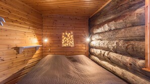 A log cabin room with a bed, a wall-mounted shelf, and a window with a light fixture.