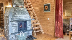 A cozy cabin interior with a stone fireplace, wooden staircase, and a wooden ceiling.