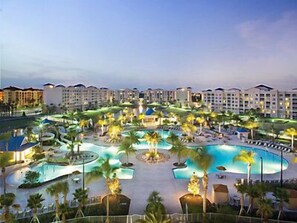 Un resort con varias piscinas, palmeras y un complejo de edificios grande al fondo.
