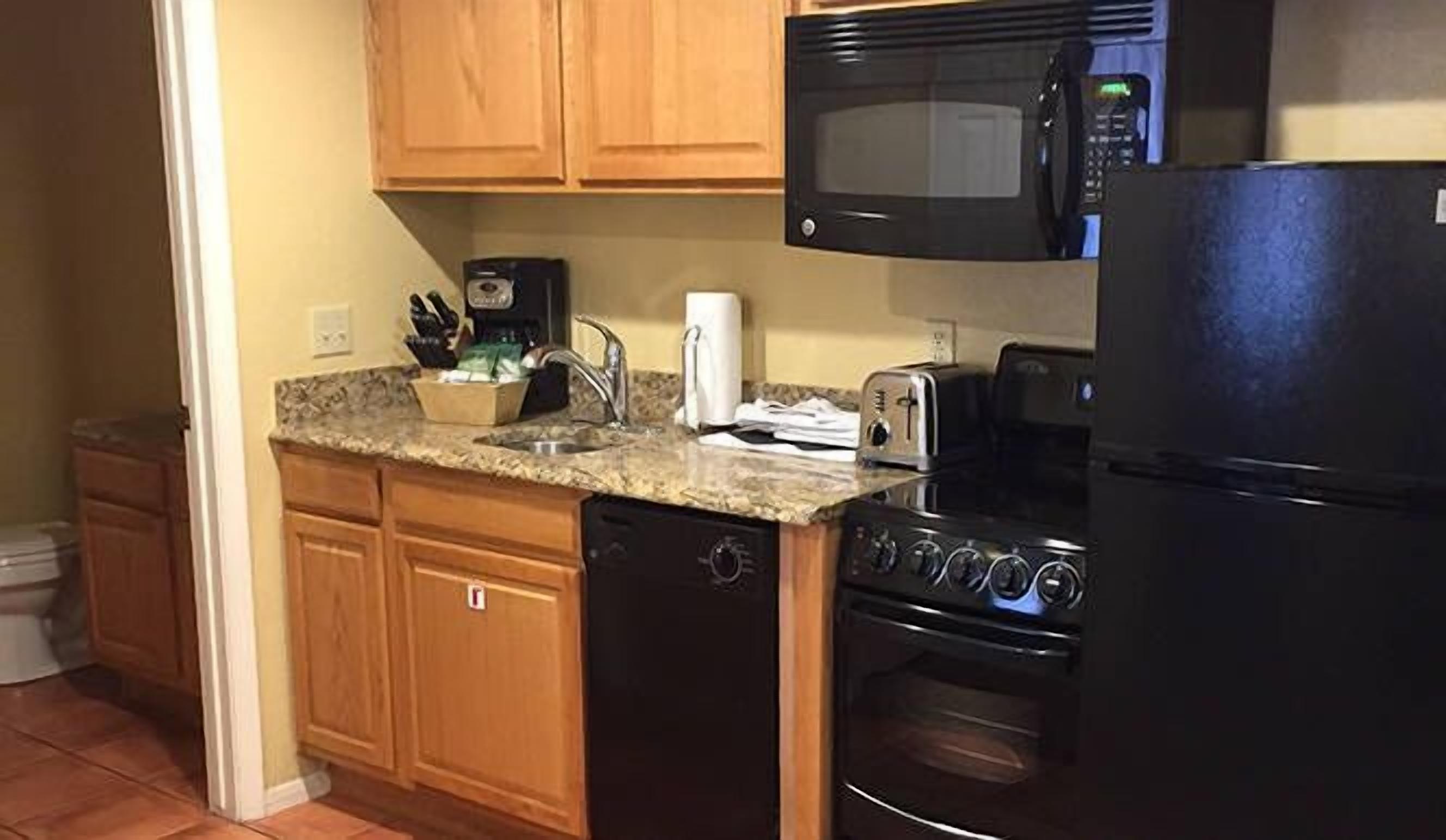 A kitchen with wooden cabinets, a granite countertop, a microwave, a toaster, a dishwasher, and a refrigerator.