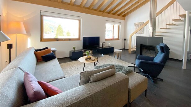 A spacious living room with a high ceiling, a sofa, a coffee table, a TV, and a fireplace. - Apartment Raber by Interhome (Churwalden)