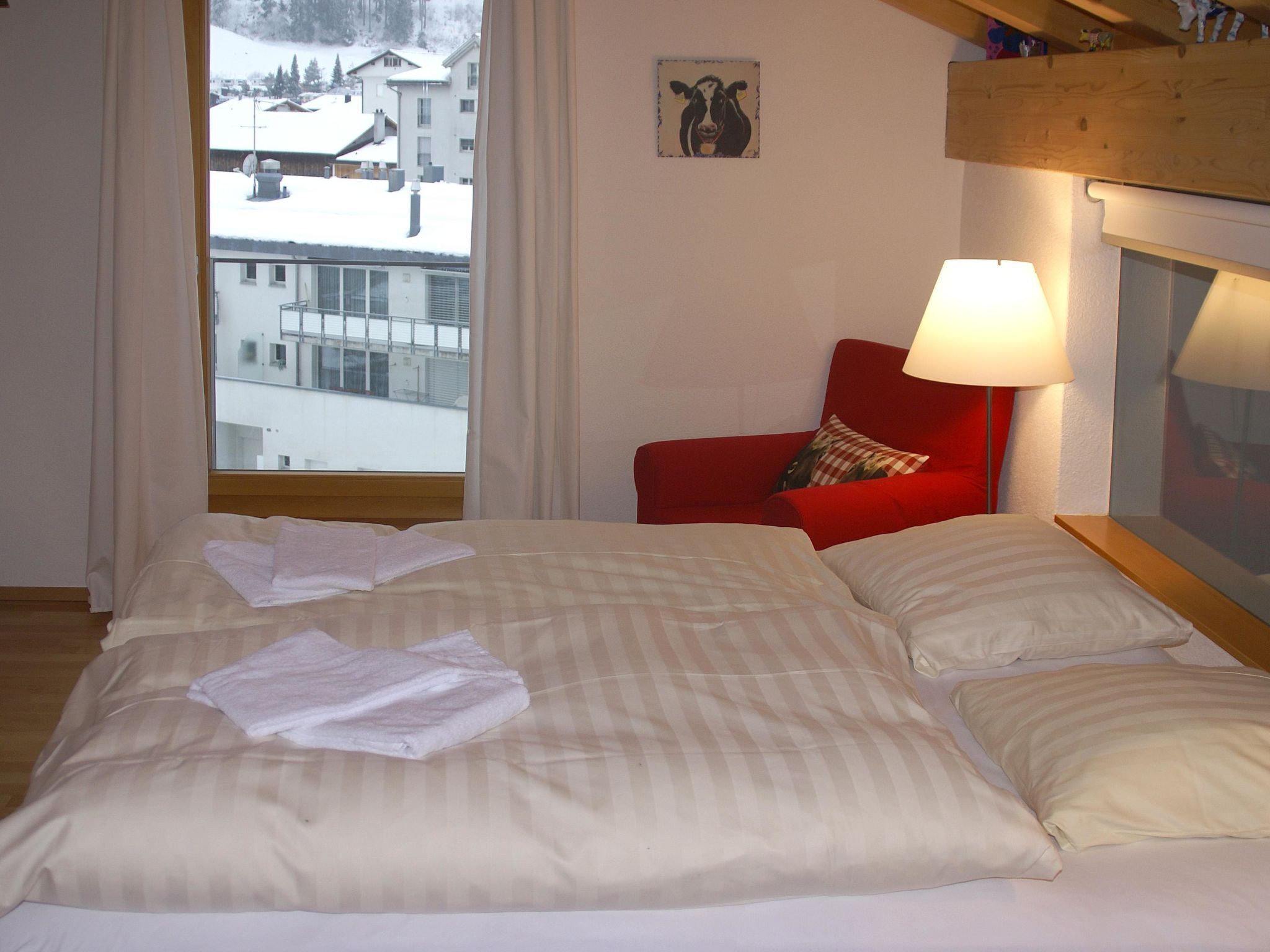 A hotel room with a bed, a red chair, a lamp, and a view of a snowy landscape.