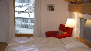 A hotel room with a bed, a red chair, a lamp, and a view of a snowy landscape. - Apartment Raber by Interhome (Churwalden)