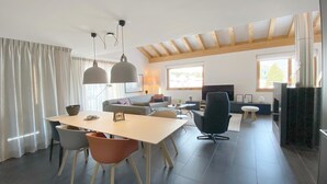 A modern living room with a dining area, wooden beams on the ceiling, a fireplace, and large windows. - Apartment Raber by Interhome (Churwalden)