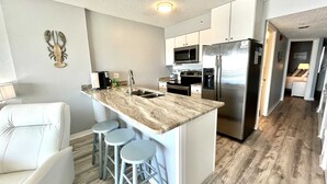 A modern kitchen with a central island, stainless steel appliances, and a seating area with a white sofa and stools.