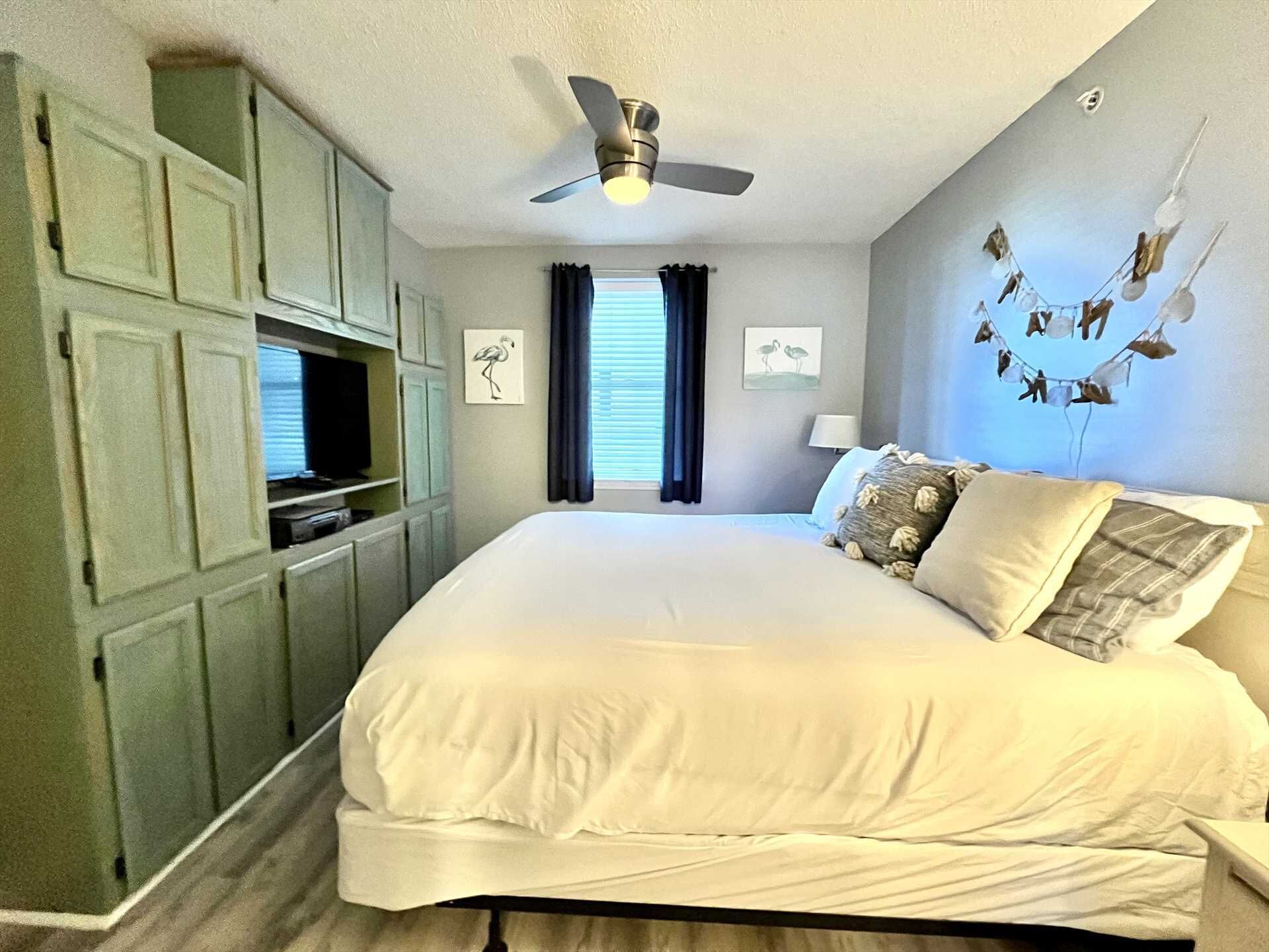 Un dormitorio con una cama grande, un ventilador de techo, un televisor y una pared decorada con pájaros.