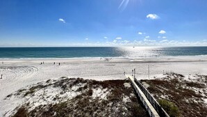 A beach with a wooden boardwalk leading to the water, clear skies, and a few people walking.