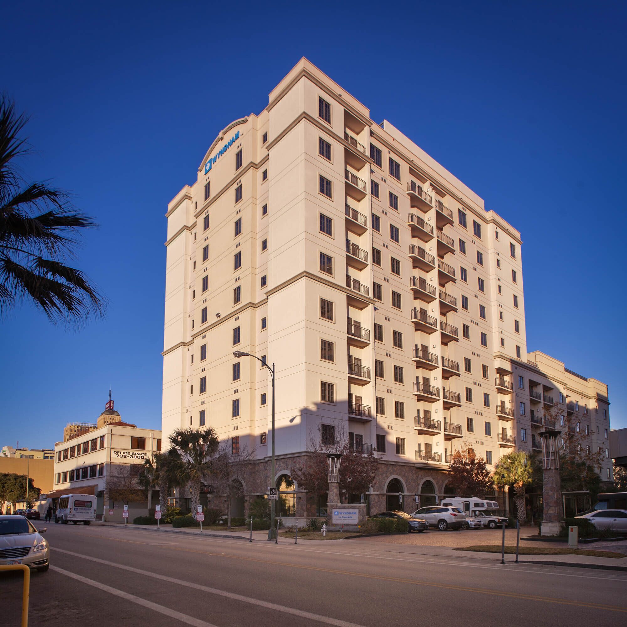 A multi-story hotel with a prominent sign at the top, a ground-level entrance, and a parking area in front.
